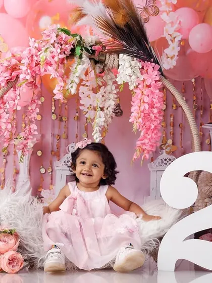 The birthday girl smiling brightly, seated in a floral hoop swing, celebrating turning two.