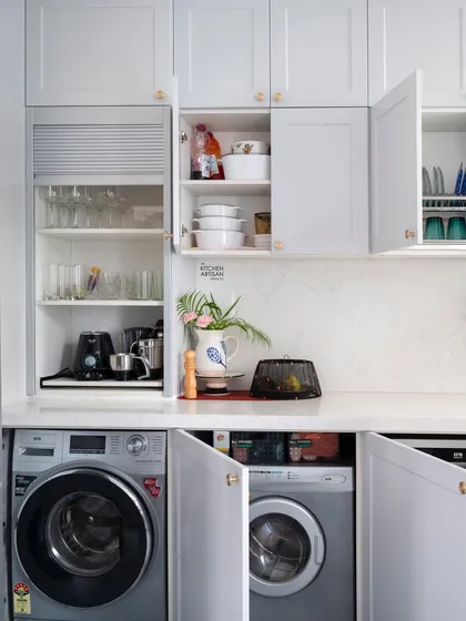 In this all-white kitchen, the washing machines are hidden behind cabinet doors, completely disappearing into the design. This allows the space to maintain its serene and uncluttered look while still being highly functional.