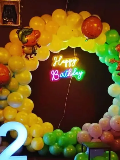 A Peppa Pig themed second birthday party with a colorful circular balloon arch and a '2' marquee light.