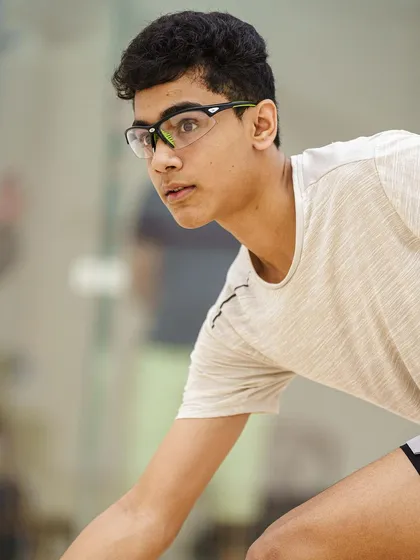 A tight portrait of Abdus Samad, showing his concentration as he prepares for a shot. The protective eyewear is a key detail of the sport, and the focus is on his determined expression.