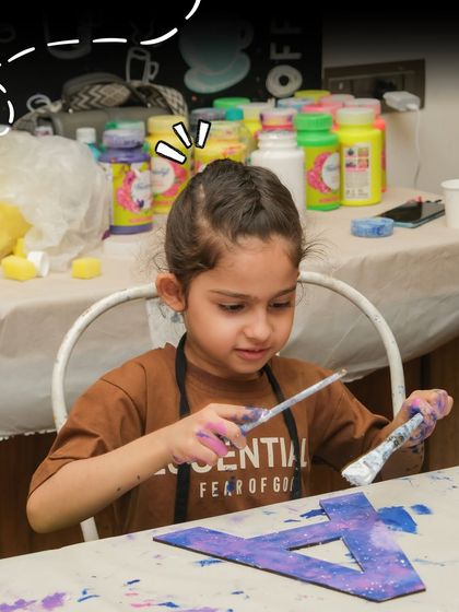 A young girl concentrates on painting her wooden initial. I provide all the materials and a supportive environment for kids to explore their artistic talents.