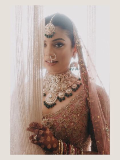 A peek-a-boo portrait of Radhika from behind a curtain. This playful yet elegant shot creates a sense of anticipation and highlights her beautiful bridal details.