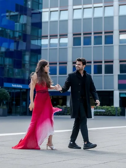 A candid walking shot through a modern plaza in London. The movement in the bride's red dress and their connected hands create a feeling of journey and effortless style.