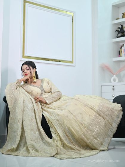 A model reclining gracefully on a sofa, the skirt of her ivory anarkali gown spread out to showcase the beautiful fabric and embroidery.