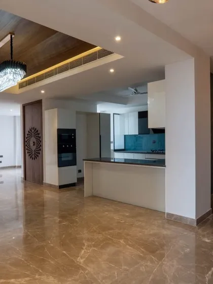 This image shows a spacious, unfurnished living area, highlighting the foundational elements of the design. The glossy marble floors, wood-paneled ceiling, and open-plan kitchen create a luxurious canvas ready to be personalized.