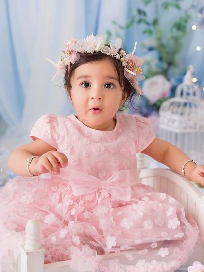 A portrait of a little princess on her miniature bed. Her wide, curious eyes and the stunning floral backdrop create a captivating image.