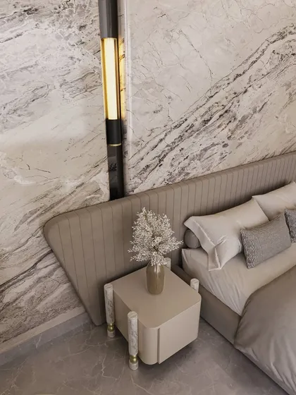 A close-up detail shows the custom bedside table and elegant wall sconce set against the dramatic veining of the marble. Every element is chosen to complement the material palette and enhance the room's luxurious feel.
