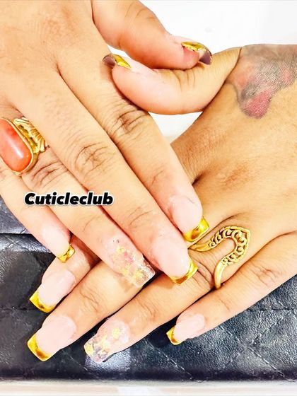 A modern interpretation of the French manicure. This set features a neutral base with bold, metallic gold tips on square-shaped extensions, along with a clear accent nail containing gold flakes.