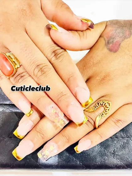 A modern interpretation of the French manicure. This set features a neutral base with bold, metallic gold tips on square-shaped extensions, along with a clear accent nail containing gold flakes.