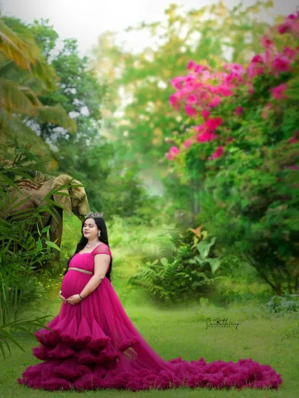 A majestic outdoor portrait in a magenta gown with a long, flowing train. The lush garden setting and the regal pose make this mother-to-be look like a queen in her natural element.