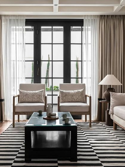 In our Riviera Maison project, we designed this family room with a comfortable, neutral-toned sofa and armchairs. The space is grounded by a bold black-and-white striped rug and features a custom black fireplace with patterned tile inserts.