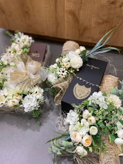 A grand gesture for a special occasion. This arrangement features multiple bottles of Dom Perignon, each beautifully wrapped and presented with lush white floral arrangements.