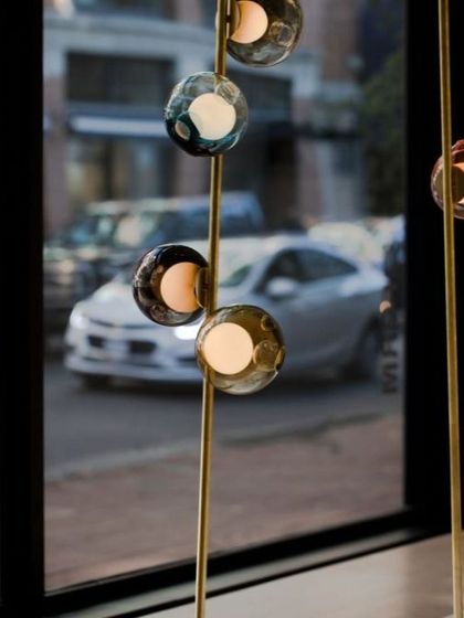 A Bocci stem installation seen from inside a showroom, with the city street visible through the window, showing how the lights interact with an urban environment.