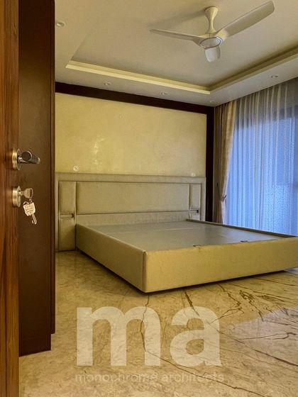 A simple and warm bedroom design, seen from the doorway. The focus is on clean lines, a neutral color palette, and the beautiful texture of the marble flooring.