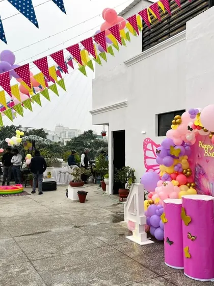 A beautiful butterfly-themed decoration for a 4th birthday party on a terrace. The setup includes a balloon arch, a custom backdrop, and colorful buntings.