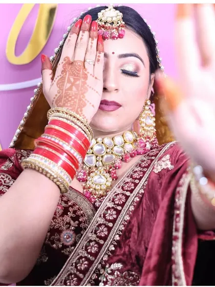 A creative bridal pose highlighting the intricate henna and the stunning polki jewellery set against the rich maroon velvet of the lehenga. The red bangles complete the traditional bridal look.