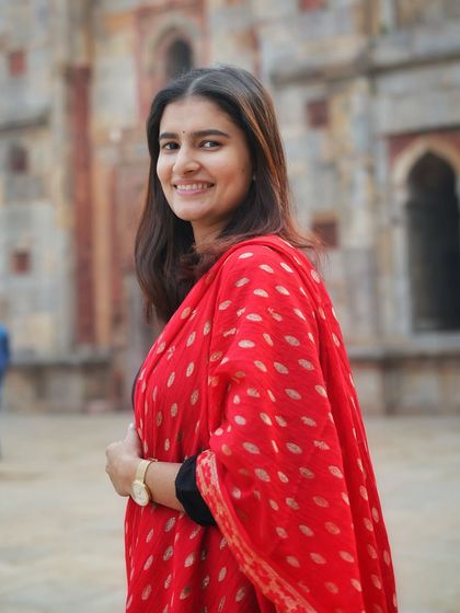 A bright, smiling portrait that perfectly captures her personality. The combination of the simple black kurta and the ornate red dupatta is a classic ethnic look.
