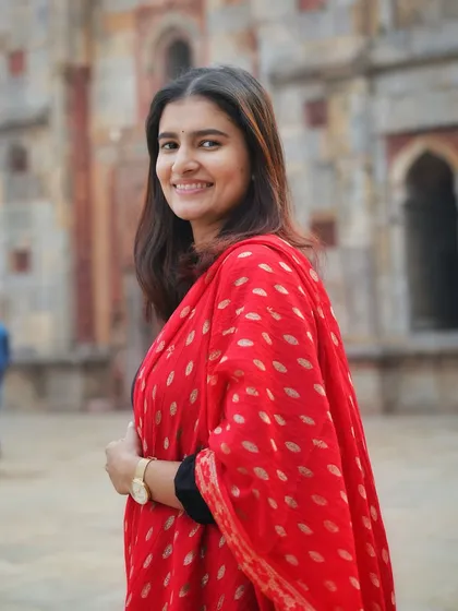 A bright, smiling portrait that perfectly captures her personality. The combination of the simple black kurta and the ornate red dupatta is a classic ethnic look.