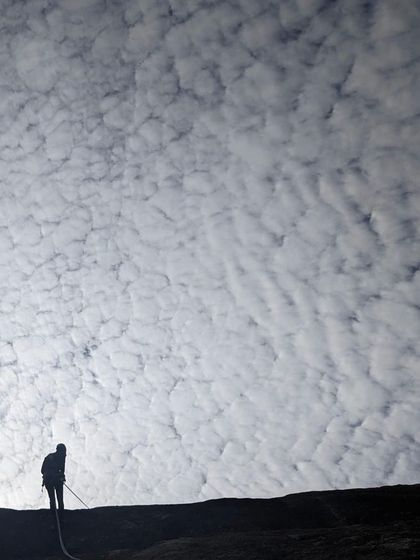 A dramatic silhouette of a climber rappelling against a mackerel sky at Hosadurga. Route development days are often filled with stunning natural beauty.