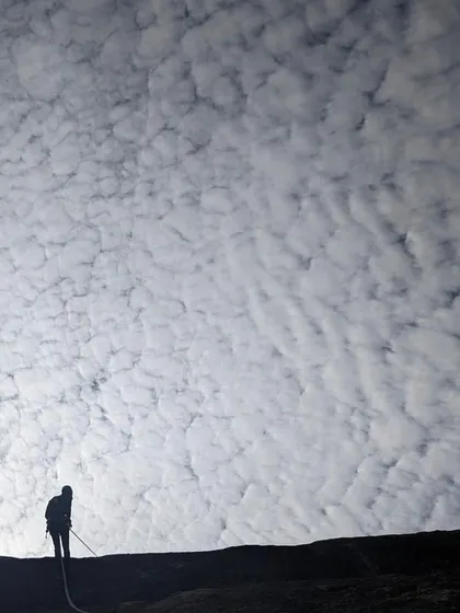 A dramatic silhouette of a climber rappelling against a mackerel sky at Hosadurga. Route development days are often filled with stunning natural beauty.