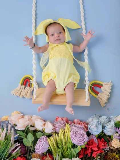 Dressed as a little bunny in a field of flowers, this newborn is ready for her first whimsical portrait on a tiny swing.