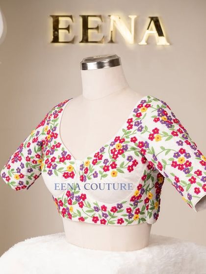A garden of flowers on a blouse. This white raw silk piece is covered in vibrant, multi-colored floral French knot embroidery, making it a cheerful and eye-catching addition to any festive wardrobe.
