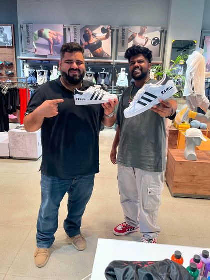 A proud customer pointing to his name, Rahul, painted on a fresh pair of Adidas Superstars. Personalization is one of our most requested services at live events.