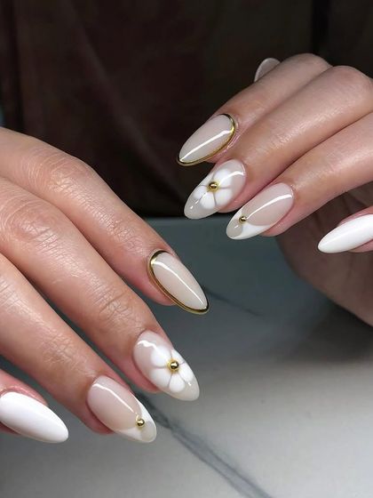 An elegant combination of white and gold. These almond nails feature a mix of solid white, a gold-lined French tip, and accent nails with 3D white flowers and gold beads.