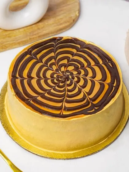 A top-down view of a butterscotch cake with an intricate chocolate and caramel glaze design. This angle highlights the beautiful decoration on the cake.