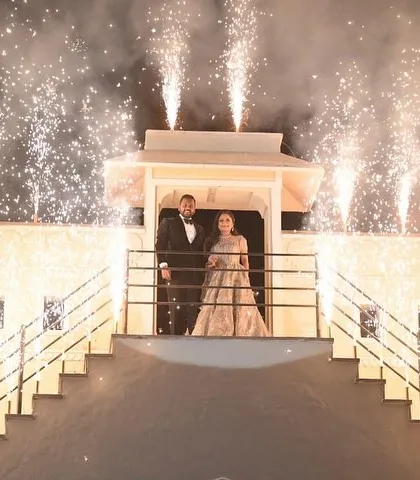 A spectacular and grand entrance for a pre-wedding celebration. The couple stands on a balcony illuminated by a cascade of fireworks, creating a truly cinematic and unforgettable moment.