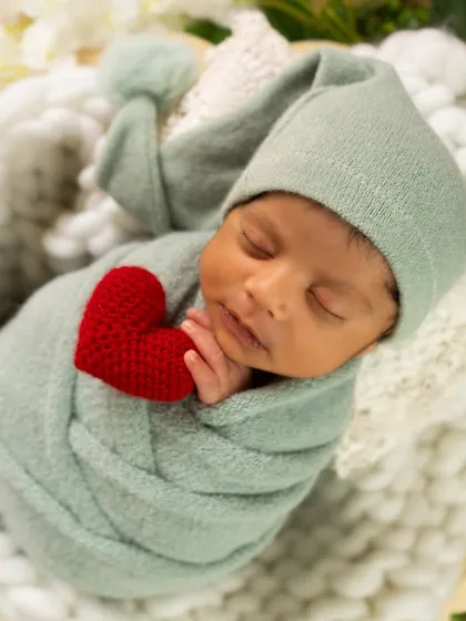 A close-up shot of a sleeping baby in a sage green wrap, holding a small red heart. This simple pose highlights the baby's peaceful features.