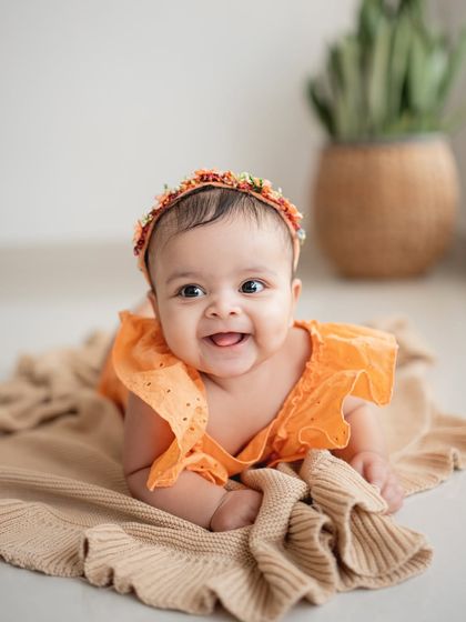 A happy baby during her sitter session. The bright orange outfit and floral headband add a fun pop of color.