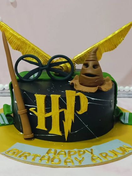 A magical Harry Potter-themed cake. This black cake is adorned with a fondant sorting hat, golden snitch, and Harry's glasses and wand.