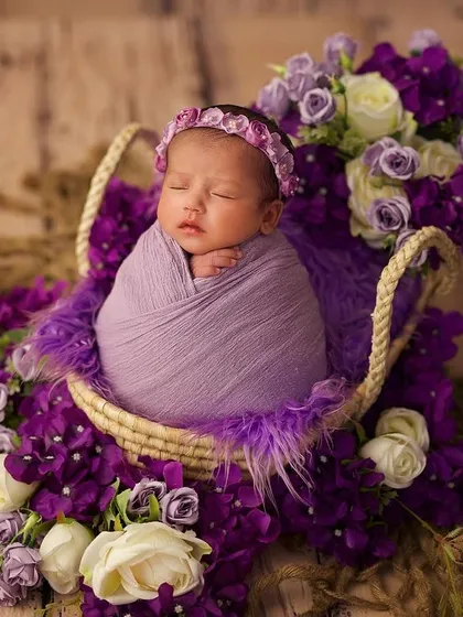 This little one is surrounded by a basket full of purple and white roses, creating a rich and beautiful floral portrait.