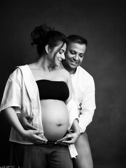 A casual and intimate black and white portrait. The focus is purely on their connection and the beautiful baby bump.