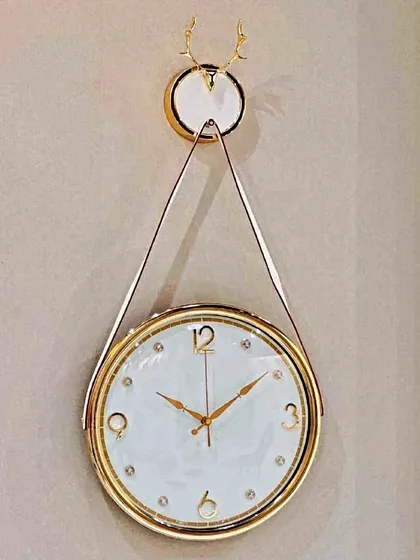 This unique hanging-style wall clock offers a fresh take on timekeeping. The white and gold clock face is suspended from a decorative mount, creating a light and elegant look that feels both modern and timeless.