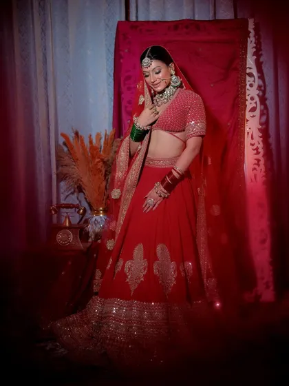 A full-length portrait of a bride in a classic red lehenga, with soft, diffused lighting creating a dreamy effect.