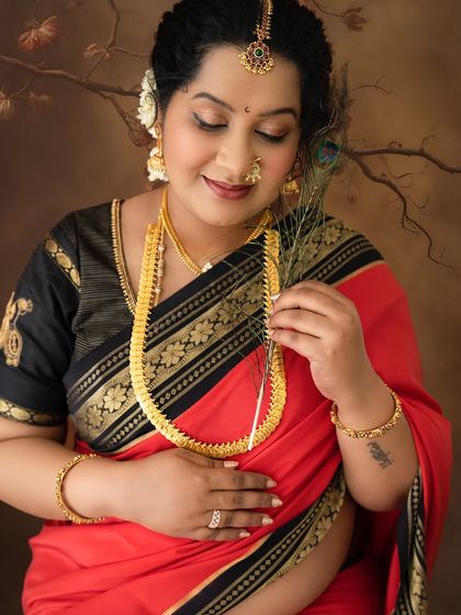 A close-up shot focusing on the serene expression of a mom-to-be in a traditional saree, holding a peacock feather, a symbol of beauty and grace.