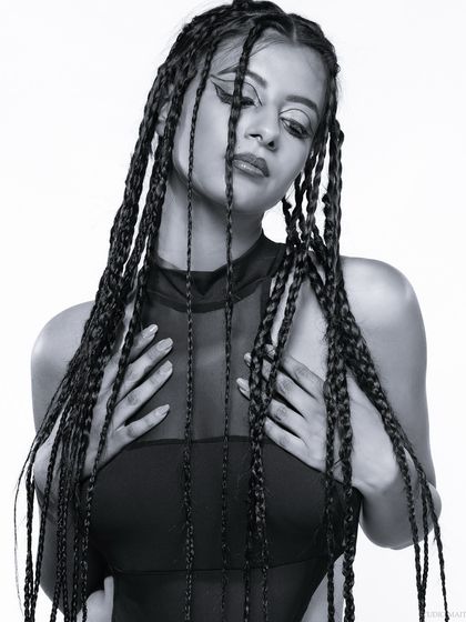 A black and white portrait of a model with braids, her hands framing her face.