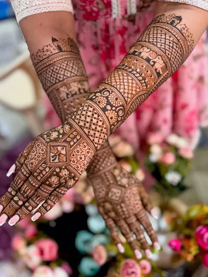 This is a classic full-coverage bridal mehendi, featuring incredibly detailed traditional patterns, including symbolic elephants and intricate geometric work extending up the forearms.