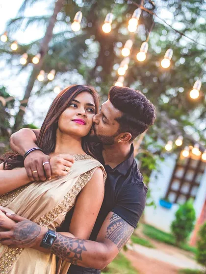 An intimate pre-wedding photo of a man kissing his partner's cheek under a canopy of warm string lights. This shot reflects our skill in using lighting to create a romantic and cozy atmosphere.