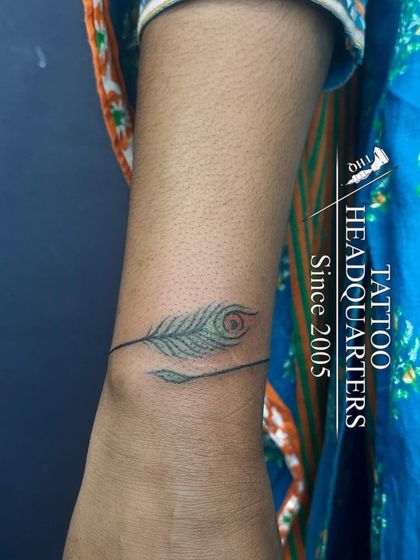A minimalist yet meaningful tattoo of a peacock feather, often associated with Lord Krishna, wrapping delicately around the wrist.