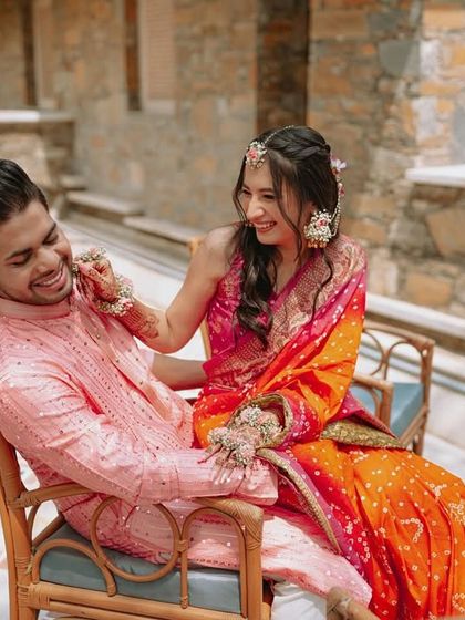 A candid moment of the couple sharing a laugh on a chair, capturing the lighthearted and joyful spirit of their Haldi.