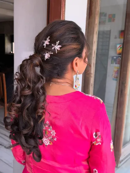 A fun and flirty high ponytail with lots of volume and curls. The dragonfly clips add a whimsical touch, perfect for a daytime event.