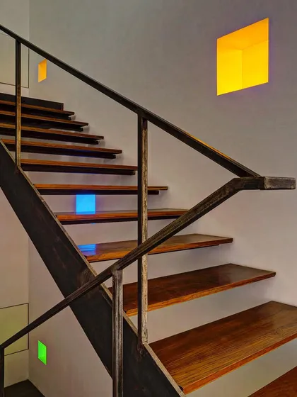 This staircase combines warm wood treads with a raw steel stringer and handrail. The small, colored light niches embedded in the wall add a playful and artistic touch to a functional element.