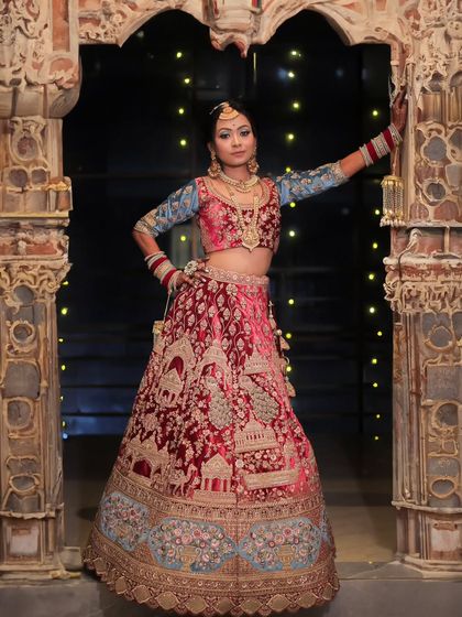 A full-length portrait of a bride in a magnificent red and blue lehenga, posing in an ornate, palace-like doorway. This shot is all about grandeur and bridal elegance.