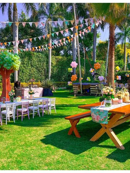 Another view of the outdoor dining setup, with rustic wooden picnic tables and colourful bunting flags strung between the palm trees, adding to the festive, garden party atmosphere.