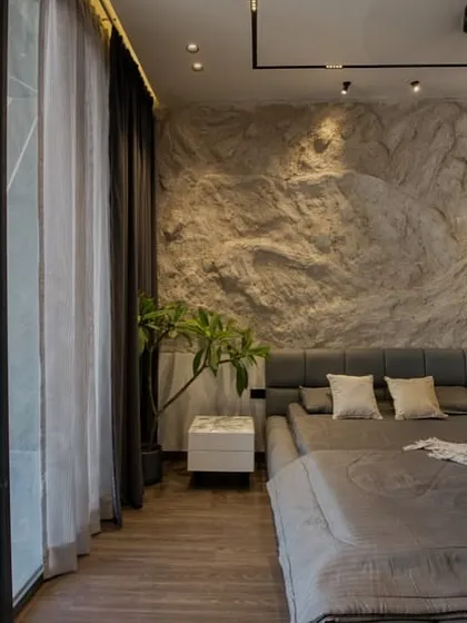 This bedroom showcases an industrial-chic aesthetic with a dramatic, custom-made textured rock wall as the headboard. Floor-to-ceiling windows connect the raw, indoor textures with the view outside.