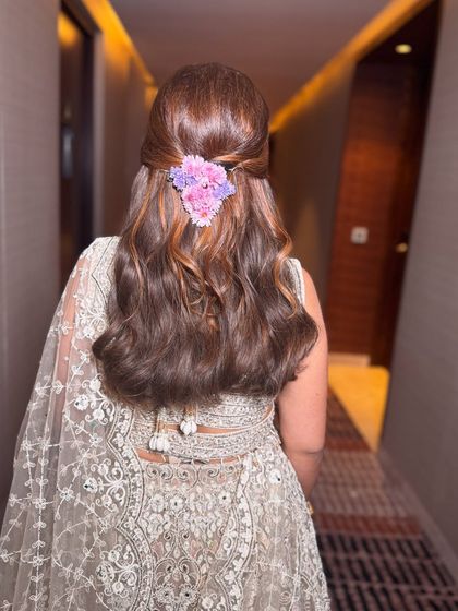 A beautiful half-up hairstyle with a floral accessory. The soft waves and the pop of color from the flowers make this a perfect look for a wedding guest.