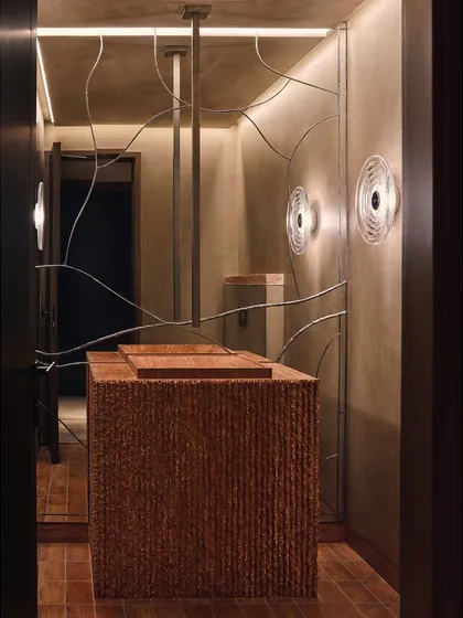 This powder room features a highly textured, custom-designed vanity that feels like a monolithic sculpture. The organic metalwork on the wall adds an artistic, linear contrast to the space.
